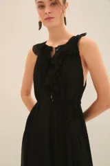 Vestido largo de gasa color negro, con escote profundo adornado con volados, lazos en el cuello con terminaciones metálicas y corte en la cintura con cinturón a tono.