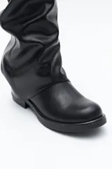 Bota de caña alta color negro, con diseño utilitario, puntera redondeada y taco bajo. Presenta un efecto fruncido en la caña y tres hebillas metálicas decorativas.