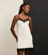 Camisón corto de color blanco, con escote en V adornado con encaje negro y tirantes finos ajustables. El ruedo también está decorado con un borde de encaje negro.