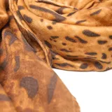 Pashmina rectangular color camel con estampado floral multicolor, terminada en pompones decorativos.