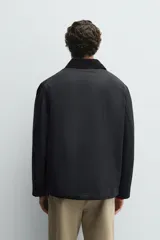 Parka de corte relajado en color negro, confeccionada en tejido de algodón con interior ligeramente acolchado. Presenta cuello de solapa en pana, cierre frontal con cremallera y bolsillos delanteros tipo plastrón con solapa y botones a presión.