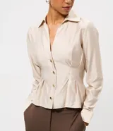 Camisa de manga larga confeccionada en satén color beige, con cuello clásico, cierre frontal de botones y pliegues decorativos en la cintura que realzan la silueta.