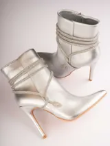 Botines plateados con terminación en punta y taco aguja. Decorados con tiras de strass que se enrollan alrededor del tobillo y se atan en el empeine.