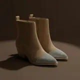 Bota texana de gamuza color beige, con puntera en punta decorada con strass plateado. Presenta un diseño de caña media con elásticos laterales y taco cuadrado de estilo western.