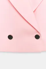 Blazer corto rosado con cuello solapa, hombreras y mangas largas. Cuenta con cierre cruzado delantero con dos botones oscuros y un bolsillo de ojal en el pecho.