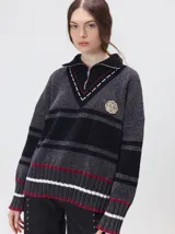 Pullover de punto con textura aterciopelada, diseño oversize, cuello polo con cierre frontal parcial y detalles de pespuntes en contraste. Presenta rayas horizontales en tonos tierra y un parche bordado con la letra M en el pecho.