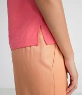 Blusa blanca de poliéster con cuello redondo, mangas cortas, cierre trasero en forma de gota, pequeñas aberturas laterales y acabados en pespuntes en las mangas y el cuello.