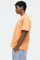Remera de algodón de peso medio, color naranja, con cuello redondo ribeteado y hombros caídos de corte relajado.