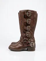 Bota de caña alta en cuero sintético color chocolate, con diseño de múltiples hebillas metálicas laterales y detalle de herrajes en el tobillo. Cuenta con taco cuadrado bajo y suela de goma.