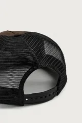 Gorra trucker marrón con visera plana y red negra en la parte trasera. Cuenta con un bordado rojo en el frente con la inscripción "Indie Behaviour 1975" y otro bordado blanco en el lateral que dice "Committed to the bands".