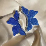 Par de aros con forma de media flor, color azul brillante con detalles de strass y gancho de acero quirúrgico.