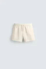 Short de baño de color beige con textura seersucker, cintura elástica con cordón ajustable, bolsillos laterales y forro interior.