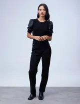 Pantalón negro de tiro alto y corte recto, confeccionado en tejido elastizado. Presenta un diseño frontal con botones decorativos aplicados en los laterales de la cintura y costuras verticales que estilizan la silueta.
