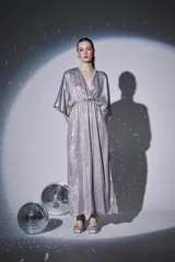 Vestido largo de fiesta en color plateado con acabado brillante. Presenta escote en V cruzado, mangas tipo kimono 3/4 y cintura elástica con frunces que dan caída fluida a la falda.