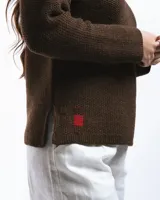 Buzo de lana merino con cuello bote y mangas largas. Presenta un detalle bordado a mano en color azul en la parte inferior.