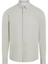 Camisa de vestir gris claro, de corte slim, con cuello clásico, cierre frontal con botones y mangas largas. Presenta el monograma de Calvin Klein bordado en el pecho.