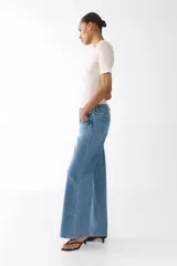 Jean de tiro alto con corte wide leg, confeccionado en denim de algodón con leve elasticidad. Presenta diseño clásico de cinco bolsillos, cierre frontal con botón y acabado en tono azul medio.