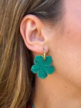 Aros colgantes con argolla dorada de acero y dije en forma de flor verde con acabado brillante y efecto con purpurina.