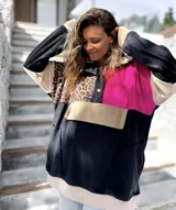 Buzo de estilo canguro con diseño color block que combina paneles en negro, fucsia, beige y un estampado de leopardo. Presenta cuello con cierre de botones a presión y un bolsillo frontal tipo canguro.