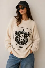 Sweater de punto color crudo, con cuello redondo, mangas largas y diseño oversize. Presenta un bordado artesanal en negro en el frente con la ilustración de un león y la inscripción "LEO".