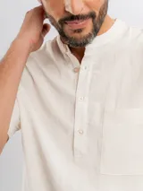 Camisa de manga corta color beige, con cuello mao, bolsillo ojal en el pecho y cierre frontal parcial con botones.