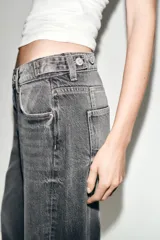 Jeans de tiro medio con diseño wide leg y cinco bolsillos. Presenta costuras verticales marcadas en el delantero y cierre frontal con cremallera y botón.