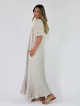 Vestido largo de lino color marrón tostado, con mangas 3/4 abullonadas, escote en V con volados y botones frontales. Cuenta con bolsillos laterales y detalle de volado en el dobladillo inferior.