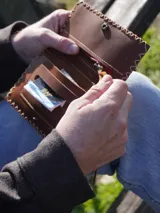 Billetera y tabaquera de cuero marrón con costuras decorativas artesanales en el contorno y cierre con botón a presión. Cuenta con compartimentos interiores para accesorios y tarjetas.