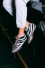 Botines acordonados con estampado de cebra en blanco y negro, puntera cubierta de glitter multicolor y suela plana color madera.