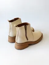 Bota corta de cuero vacuno con textura granulada, color crudo. Presenta cierre lateral metálico, suela track de goma en tono suela y tirador trasero.