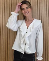 Camisa blanca de manga larga con volados en el escote en V y en los puños, con cierre frontal de botones oscuros.