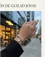 Pulsera de eslabones de acero con dije central en forma de corazón y cierre circular.