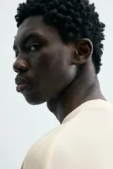 Camiseta de manga corta y cuello redondo, color crema o blanco roto, con un parche texturizado en el pecho que simula barras verticales.