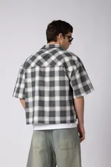 Camisa de manga corta de popelina cuadrillé en tonos marrón, blanco y gris, con diseño boxy fit, cuello camisero, cierre frontal de botones, bolsillo en el pecho con detalle bordado y dobladillo recto.