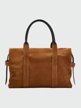 Bolso tote de gamuza color marrón, con diseño estructurado, cierre de hebilla metálica frontal y correas de hombro de cuero negro.