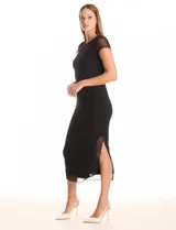 Vestido midi negro con cuello redondo, mangas cortas de microtul transparente y ruedo con acabado roulette. Presenta un forro interno opaco y una capa exterior de microtul, con un tajo lateral profundo.