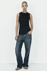 Camiseta ajustada (slim fit) color crema, con cuello redondo y mangas sisa. Presenta frunces laterales y un bajo asimétrico con detalle de encaje a tono.