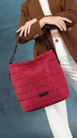 Cartera tipo tote de diseño capitoneado con patrón geométrico triangular. Presenta un acabado acolchado, asa de mano resistente y cierre superior. Incluye una etiqueta decorativa en la parte inferior frontal.