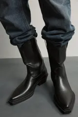 Bota estilo cowboy de color negro, con acabado liso, tiradores laterales, horma en punta, suela a tono y tacón ancho.