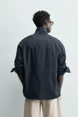 Parka de corte relajado confeccionada en tejido de algodón con efecto lavado. Presenta cuello subido, manga larga con puños abotonados, bolsillos frontales de plastrón con solapa y cintura ajustable mediante cordón interior. El cierre frontal es de cremallera oculta por una solapa con botones a presión.