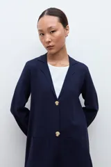 Sacón azul marino de corte largo, con cuello solapa, cierre frontal de dos botones dorados y bolsillos de parche.