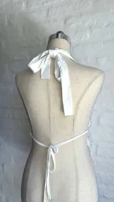 Top halter blanco con escote pronunciado en V, confeccionado en tejido transparente con lentejuelas o brillos plateados. La parte superior del busto es opaca y el resto del cuerpo es traslúcido.