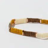 Pulsera elástica con cuentas rectangulares de colores amarillo, blanco hueso y marrón, separadas por pequeñas cuentas doradas.