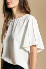 Top de manga corta con escote a la base y silueta relajada, confeccionado en tejido liviano con caída fluida. Presenta mangas amplias con volumen sutil y diseño minimalista.