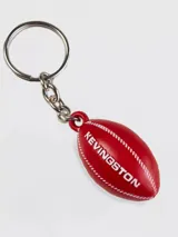 Llavero con dije en forma de pelota de rugby color rojo, con el logo de la marca Kevingston grabado en blanco.