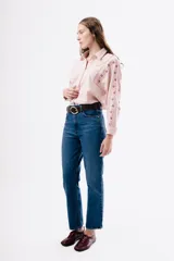 Camisa de algodón color rosado con cuello clásico y cierre frontal de botones. Presenta detalles de bordados florales en tonos rojizos a lo largo de las mangas y costuras con encaje decorativo en los hombros.