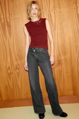 Jeans de tiro alto, color gris oscuro lavado, con pierna ancha extra larga (full length) y diseño de cintura cruzada asimétrica con cierre frontal de cremallera y botones metálicos.