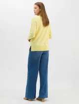 Buzo de tejido fino color amarillo, con cuello redondo, manga larga con puños acanalados y pespunte central vertical en el frente y la espalda. Presenta un ruedo ancho acanalado con tajos laterales.