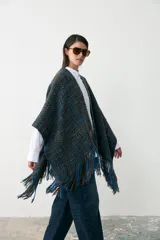 Ruana tejida en lana con diseño de trama en tonos azul y marrón, con detalle de flecos en el ruedo y parche de cuero en el frente.