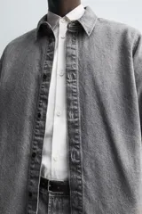 Camisa de corte relajado confeccionada en denim de algodón con efecto lavado. Presenta cuello solapa, cierre frontal con botones y mangas largas con puños abotonados.